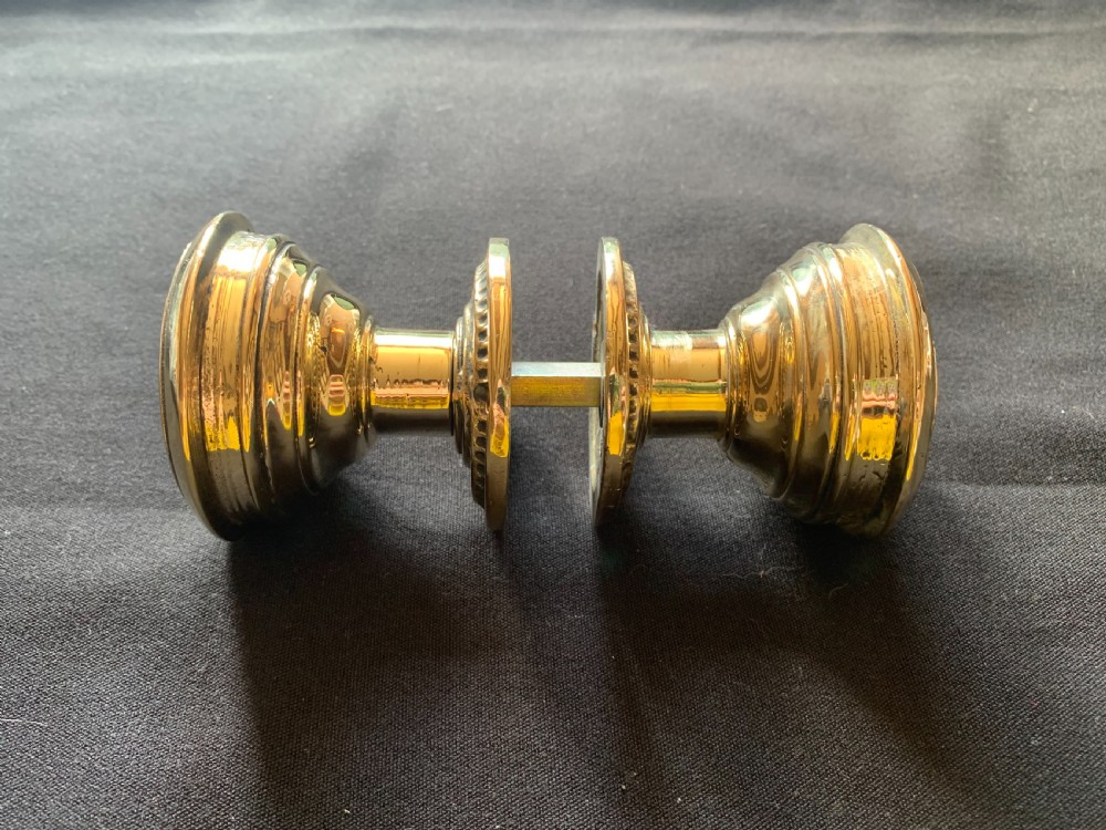 A pair of polished brass Victorian door knobs featuring raised embossed circular patterns and matching backplates. View VII