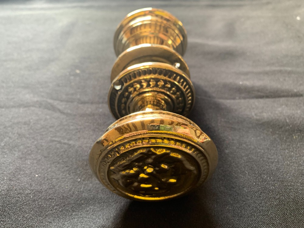 A pair of polished brass Victorian door knobs featuring raised embossed circular patterns and matching backplates. View VIII