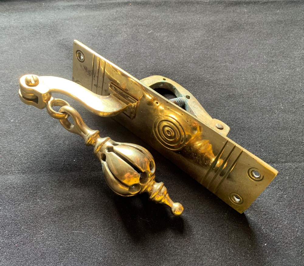 A brass Georgian mechanical doorbell pull featuring a rectangular backplate engraved with concentric circles and a bulbous drop handle.
