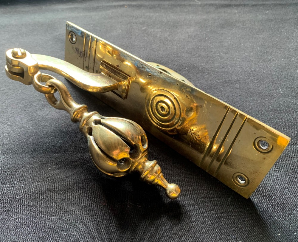 A brass Georgian mechanical doorbell pull featuring a rectangular backplate engraved with concentric circles and a bulbous drop handle. View II
