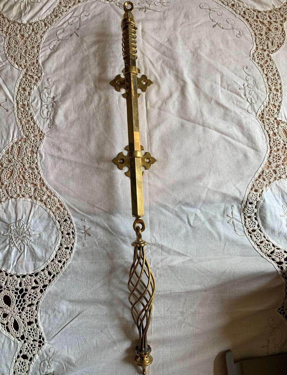 A restored Victorian mechanical door bell pull in polished brass featuring a spiral cage handle and twin decorative mounting brackets.