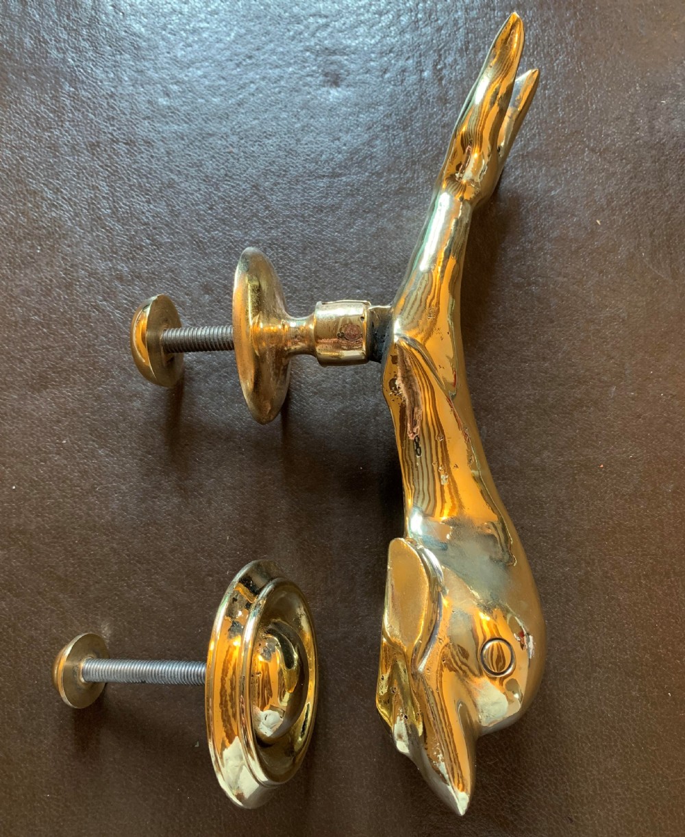 A solid polished brass door knocker styled as a Maltese dolphin, complete with a separate circular striker plate and threaded mounting bolts.