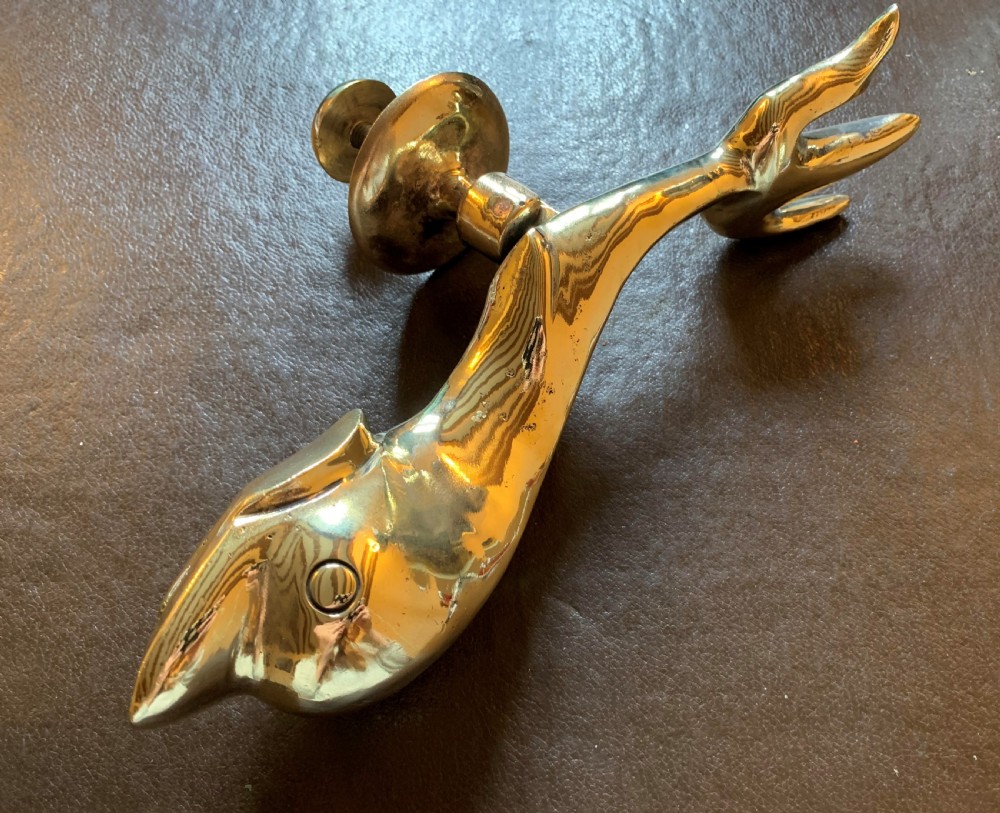 A solid polished brass door knocker styled as a Maltese dolphin, complete with a separate circular striker plate and threaded mounting bolts. View VII