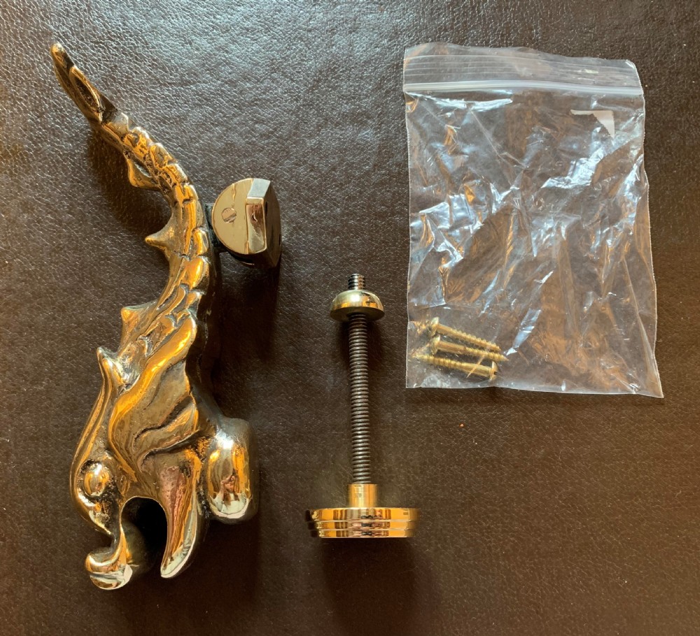 A cast polished brass door knocker sculpted in the shape of a Maltese dolphin alongside its circular striking plate and mounting bolts.