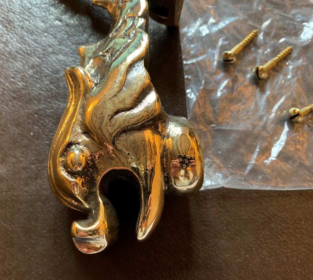 A cast polished brass door knocker sculpted in the shape of a Maltese dolphin alongside its circular striking plate and mounting bolts. View II