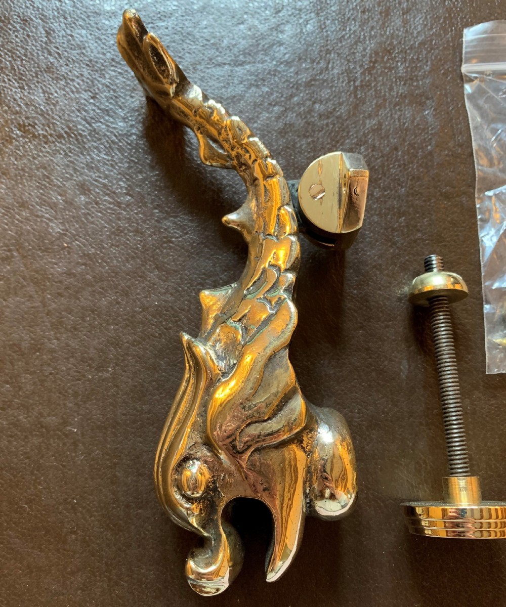 A cast polished brass door knocker sculpted in the shape of a Maltese dolphin alongside its circular striking plate and mounting bolts. View III