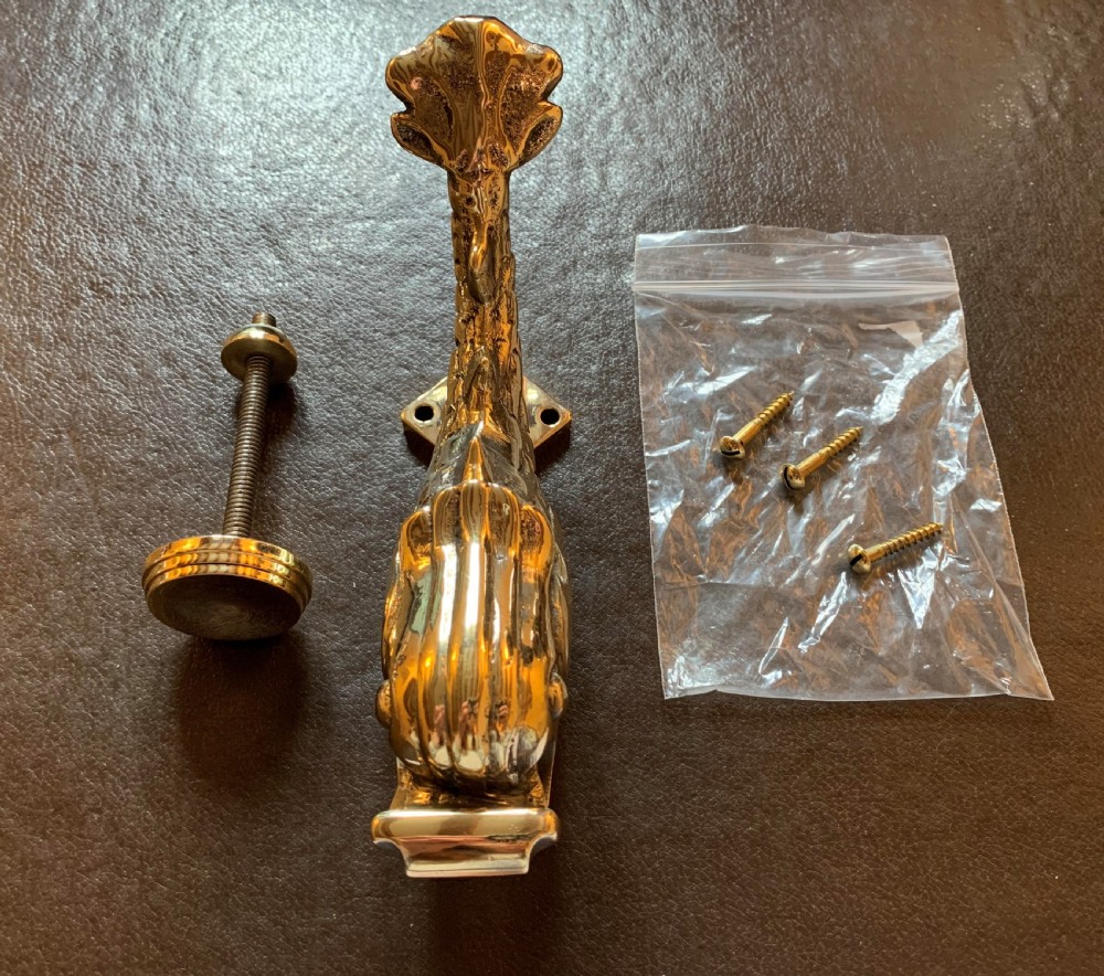 A cast polished brass door knocker sculpted in the shape of a Maltese dolphin alongside its circular striking plate and mounting bolts. View VI