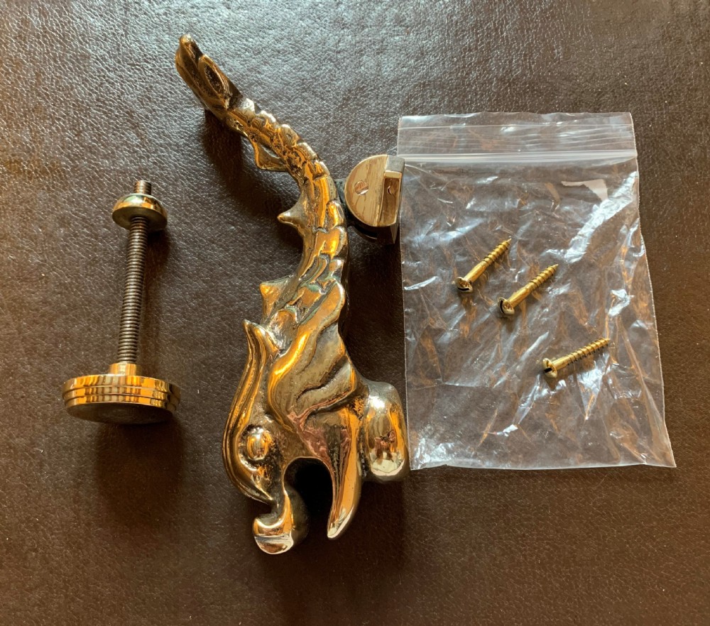 A cast polished brass door knocker sculpted in the shape of a Maltese dolphin alongside its circular striking plate and mounting bolts. View VII
