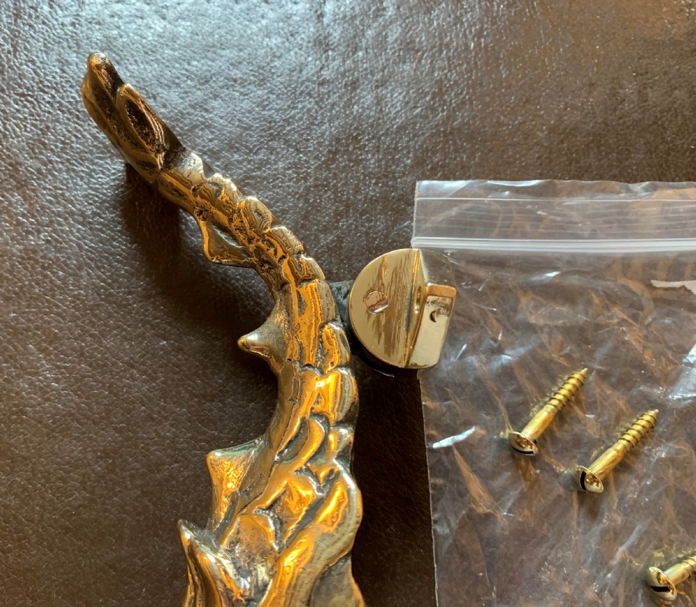 A cast polished brass door knocker sculpted in the shape of a Maltese dolphin alongside its circular striking plate and mounting bolts. View VIII