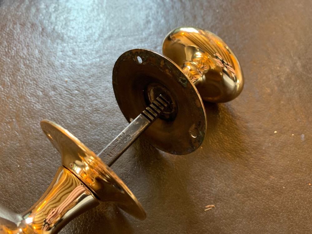 A pair of polished oval brass door knobs connected by a threaded square spindle with circular rose plates. View III