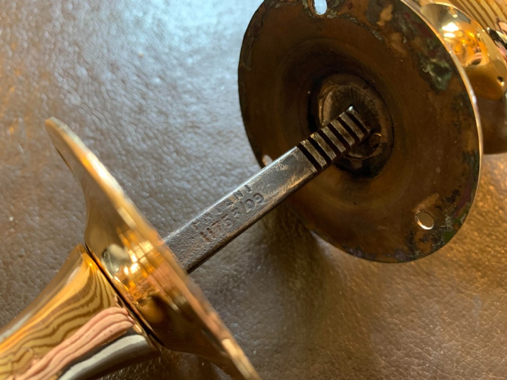 A pair of polished oval brass door knobs connected by a threaded square spindle with circular rose plates. View IV