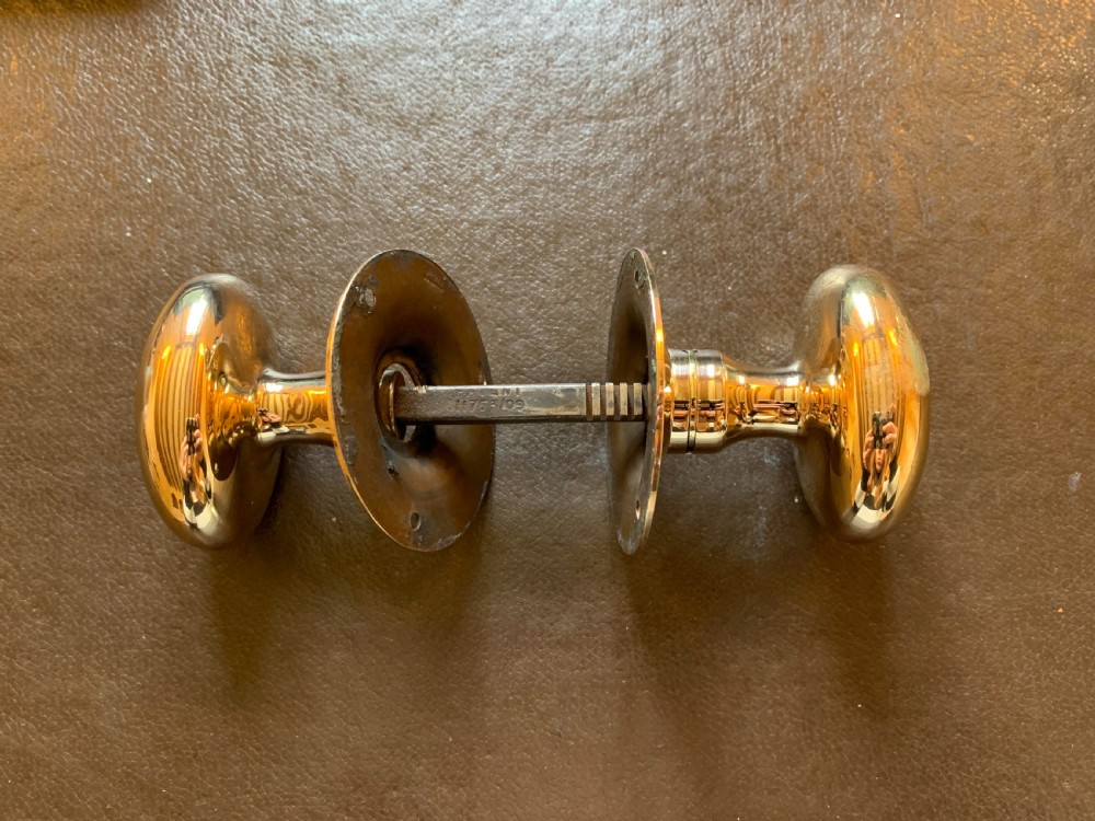 A pair of polished oval brass door knobs connected by a threaded square spindle with circular rose plates. View V
