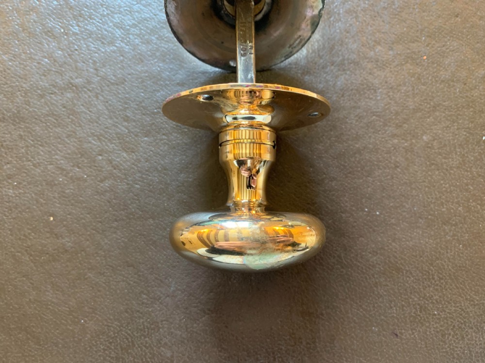 A pair of polished oval brass door knobs connected by a threaded square spindle with circular rose plates. View VI