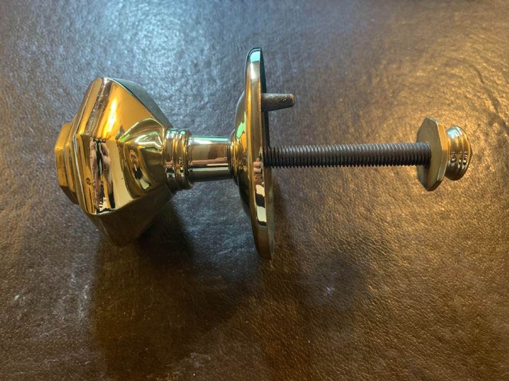 A polished brass octagonal centre door knob with a circular backplate and threaded bolt. View V
