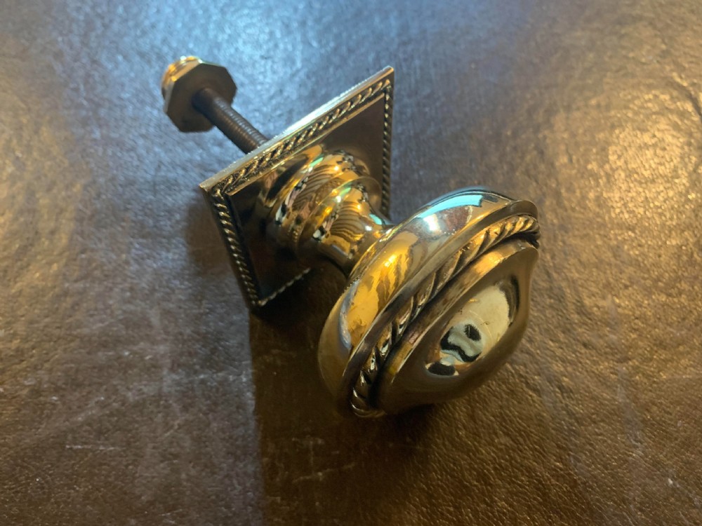 A polished Victorian brass centre door knob featuring a circular knob with a rope-twist border mounted on a square backplate. View II