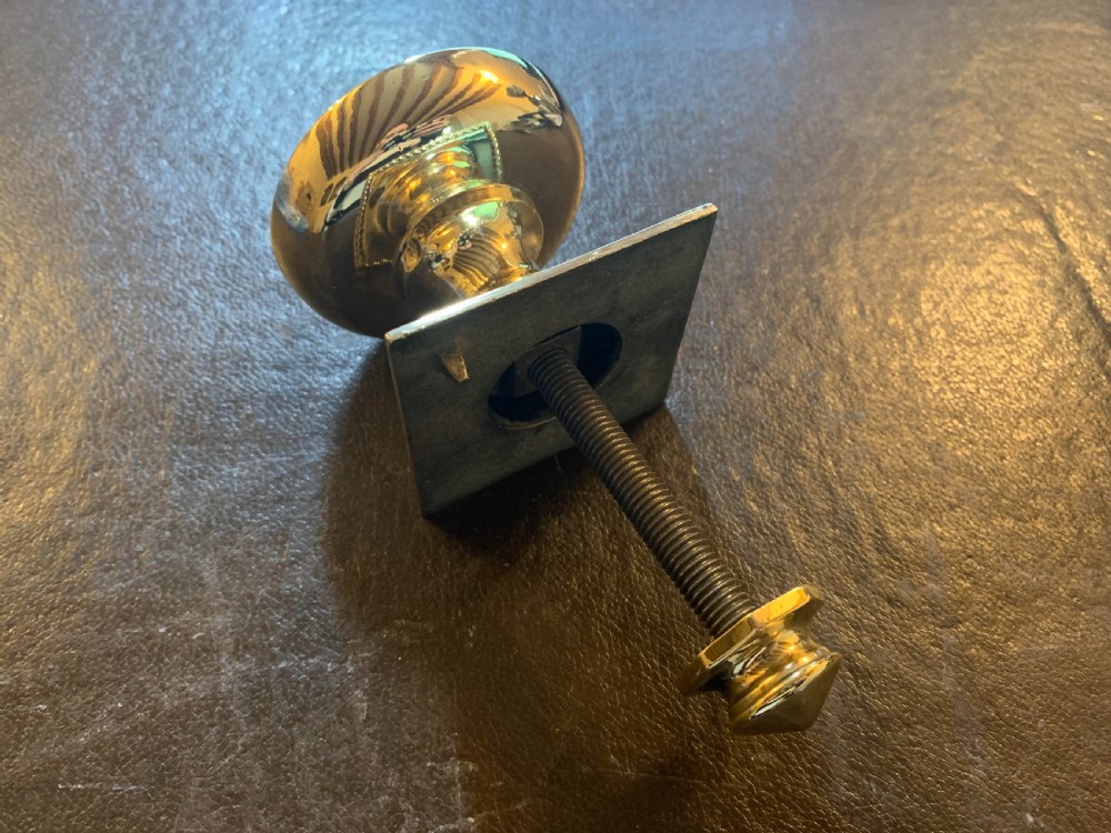 A polished Victorian brass centre door knob featuring a circular knob with a rope-twist border mounted on a square backplate. View V