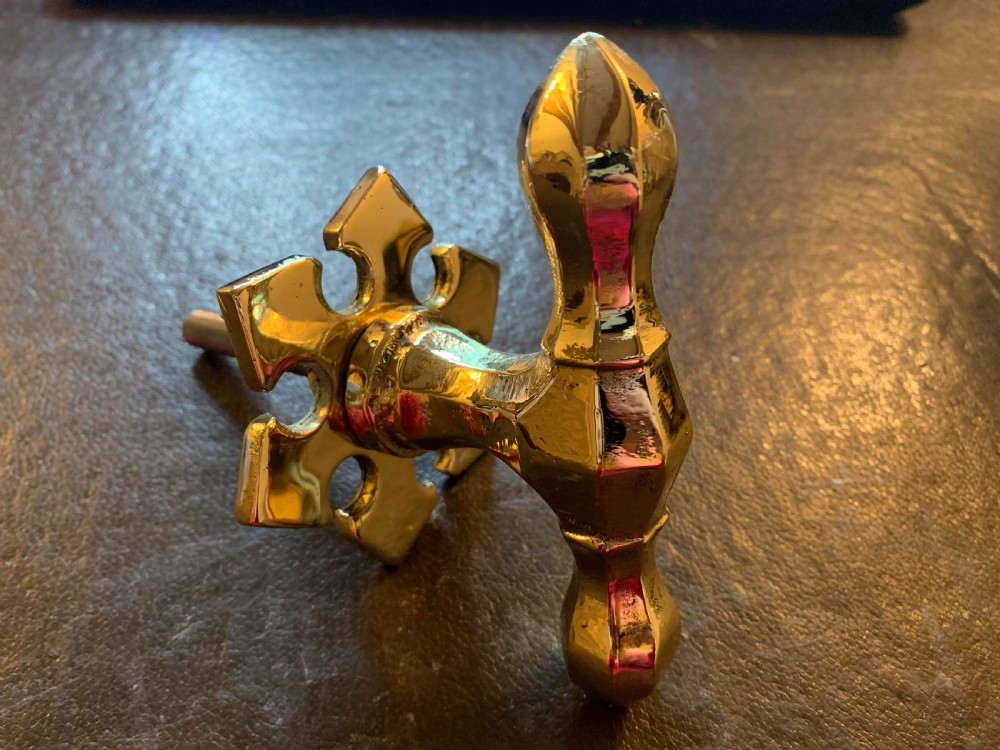 A polished brass Victorian centre door knob featuring a pointed T-bar handle and an ornate star-shaped rosette backplate with a threaded mounting bolt. View II