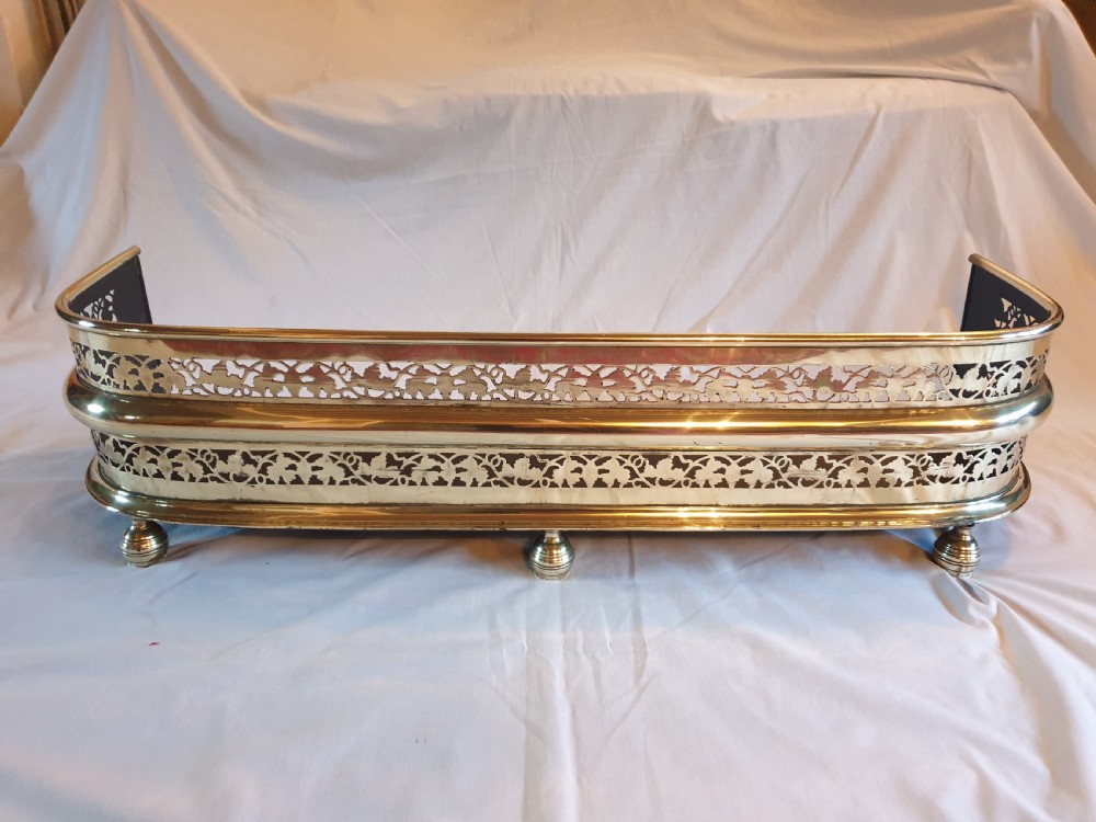 A Victorian brass fireplace fender featuring pierced fretwork patterns, rounded corners, and turned feet.