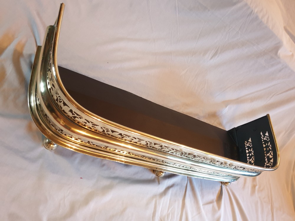 A Victorian brass fireplace fender featuring pierced fretwork patterns, rounded corners, and turned feet. View II