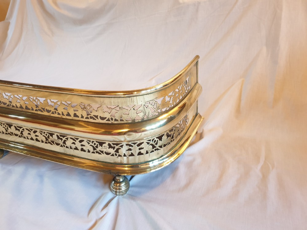 A Victorian brass fireplace fender featuring pierced fretwork patterns, rounded corners, and turned feet. View VI