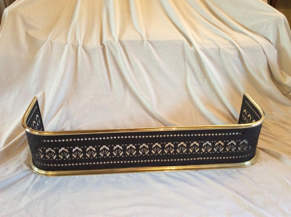 A Victorian black steel fireplace fender featuring a pierced geometric fretwork pattern framed by polished brass top and bottom rails.