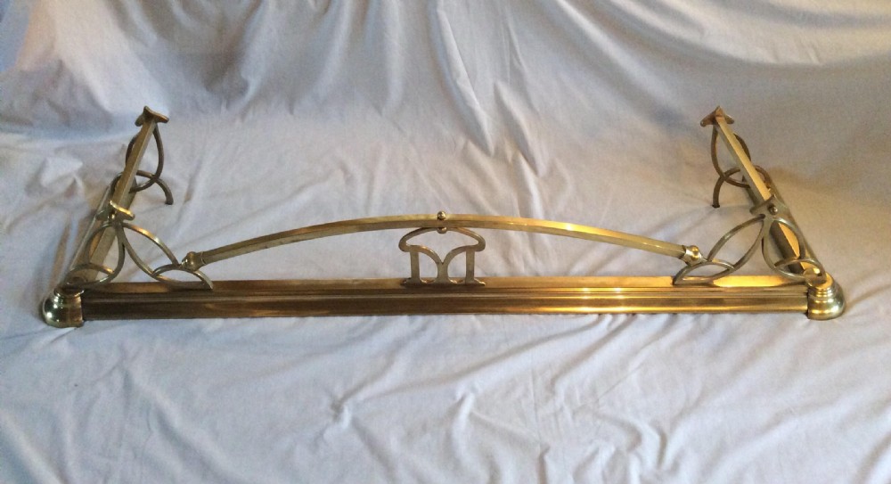 An Art Nouveau polished brass fireplace fender with an arched central rail and stylized corner motifs. View II