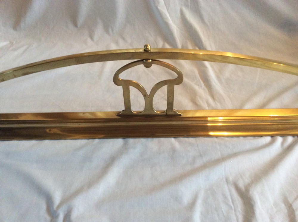 An Art Nouveau polished brass fireplace fender with an arched central rail and stylized corner motifs. View III