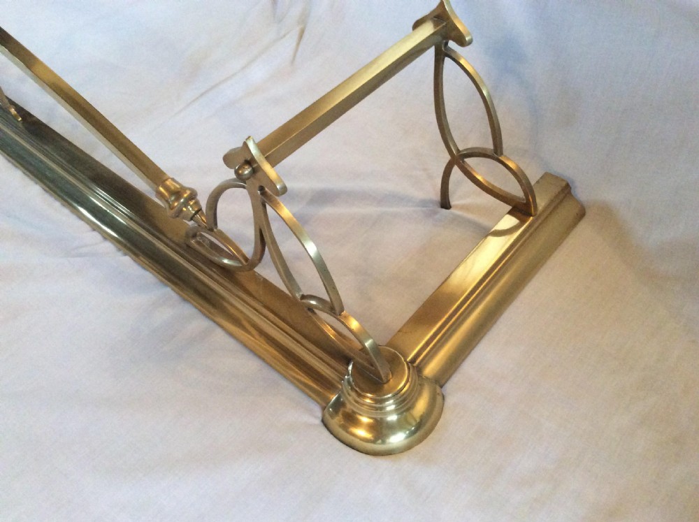 An Art Nouveau polished brass fireplace fender with an arched central rail and stylized corner motifs. View IV