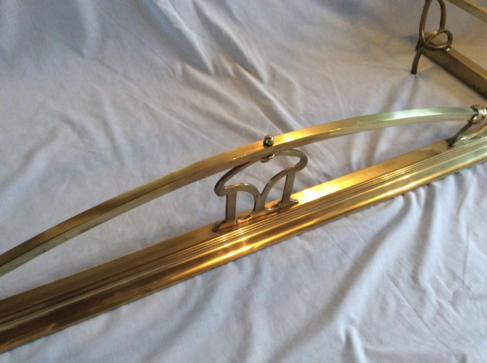 An Art Nouveau polished brass fireplace fender with an arched central rail and stylized corner motifs. View V