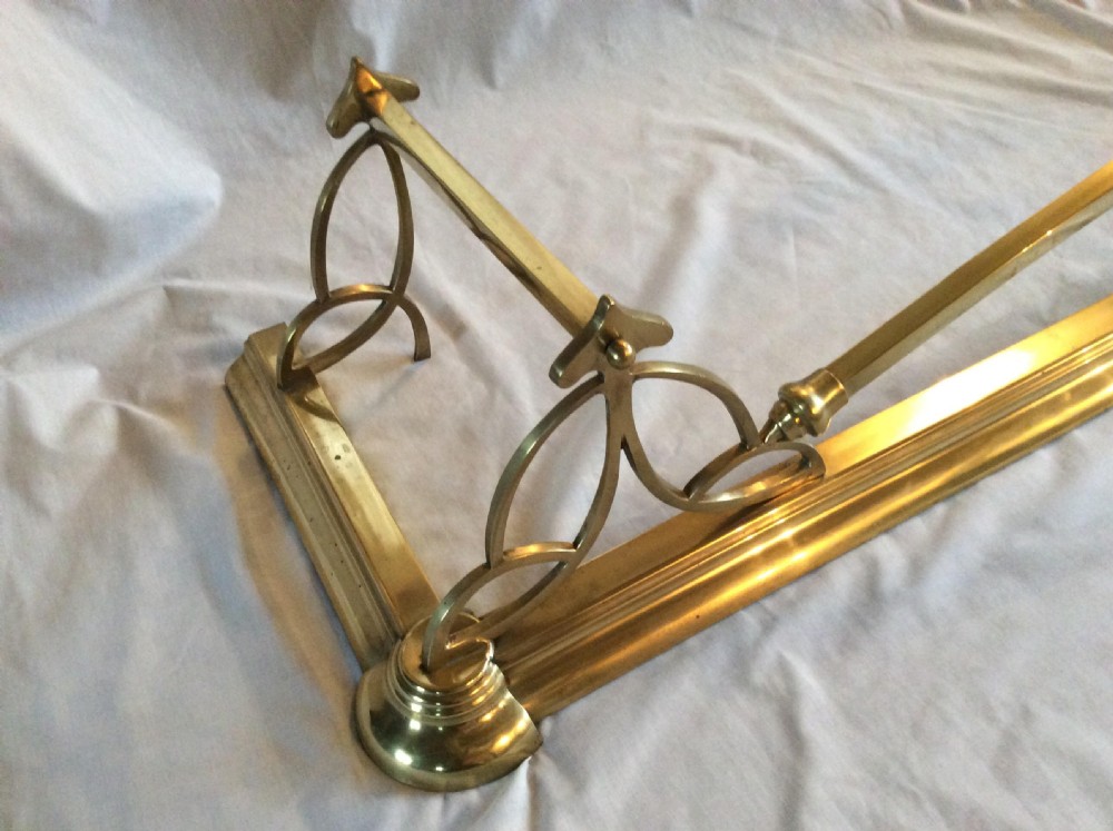 An Art Nouveau polished brass fireplace fender with an arched central rail and stylized corner motifs. View VI