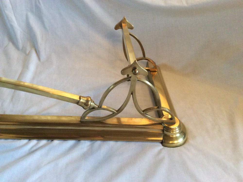 An Art Nouveau polished brass fireplace fender with an arched central rail and stylized corner motifs. View VII