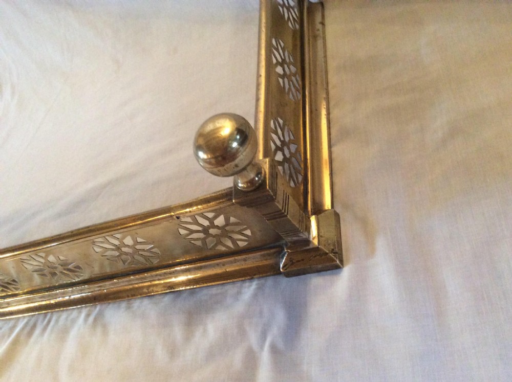 A Victorian brass fireplace fender featuring pierced floral rosette motifs along the front and side panels, finished with spherical corner finials. View IV