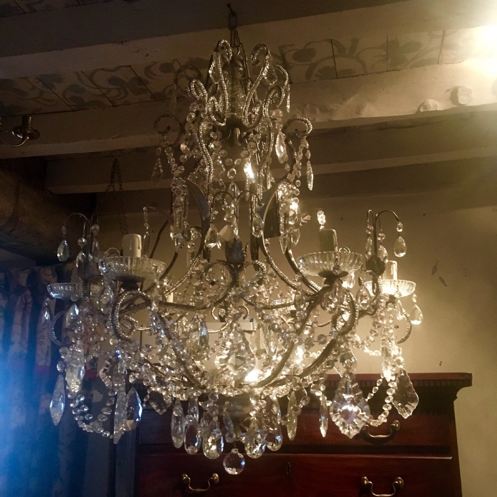 An ornate multi-tiered chandelier constructed with a scrolled metal frame adorned with cut crystal glass drops, beaded swags, and candle sleeve fittings.