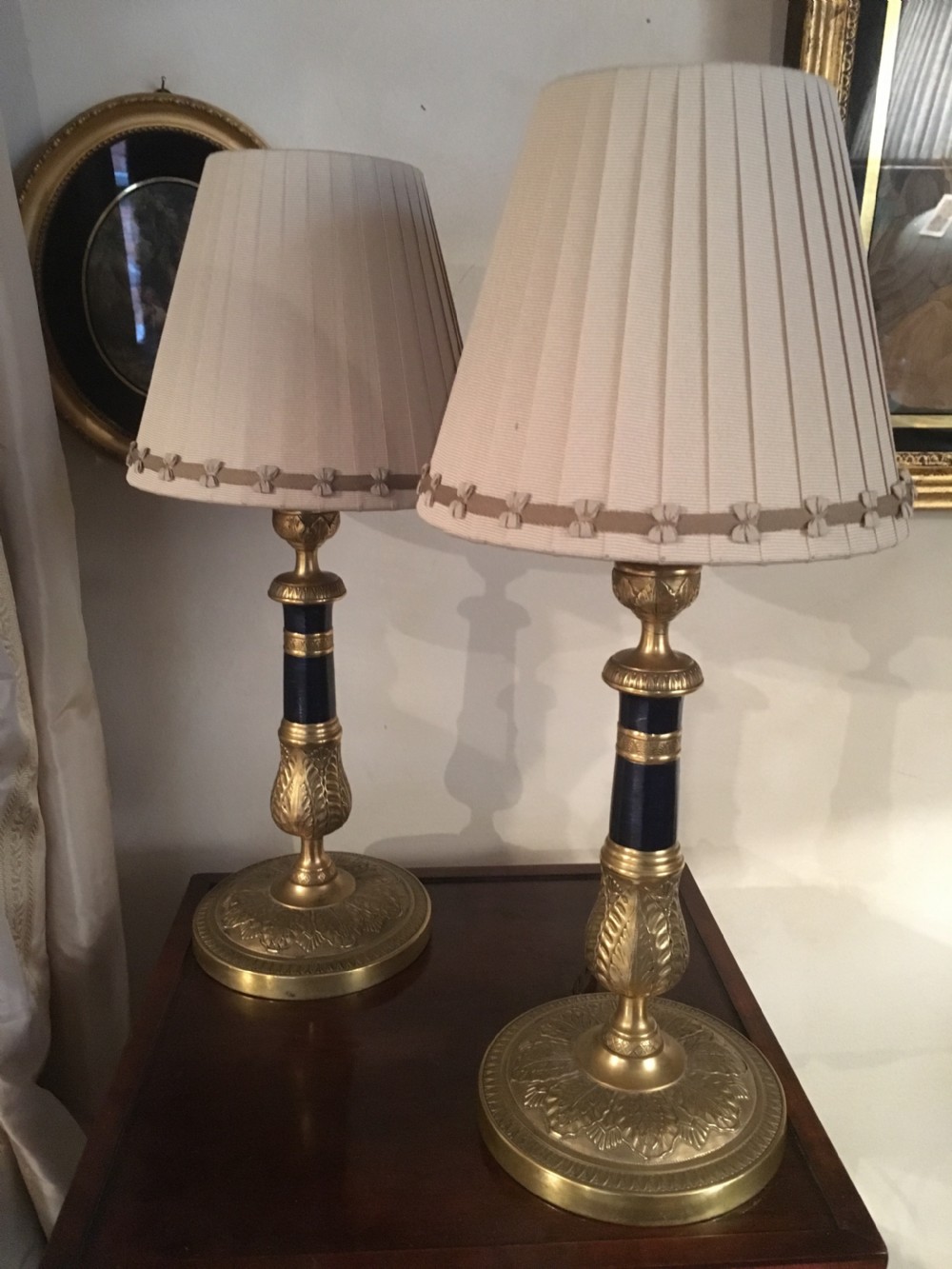 A pair of gilt brass Empire style table lamps with dark blue central columns and pleated cream fabric shades.