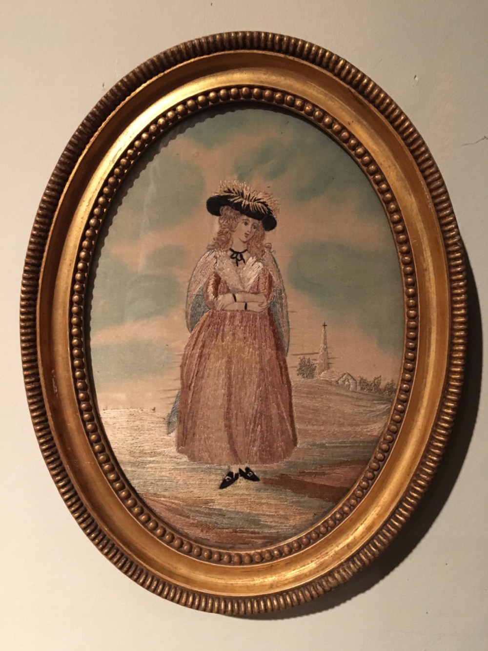 An 18th-century oval needlework picture featuring a lady in Georgian costume framed in a beaded water-gilded wood frame.