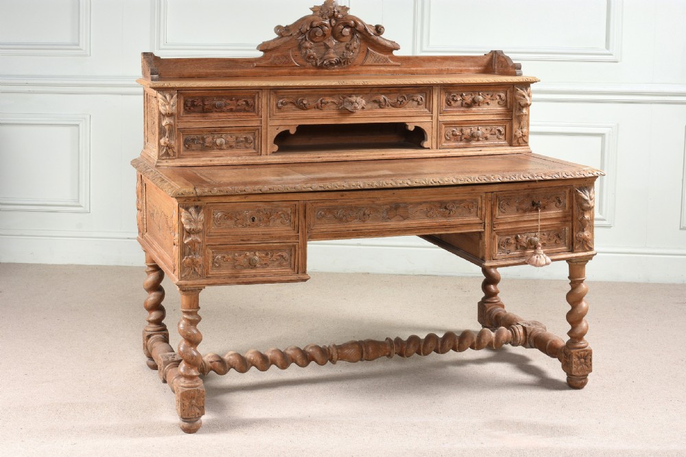 A carved oak writing desk featuring a top shelf with small drawers, an ornate crest, a pull-out writing surface, and barley twist legs connected by stretchers. View II