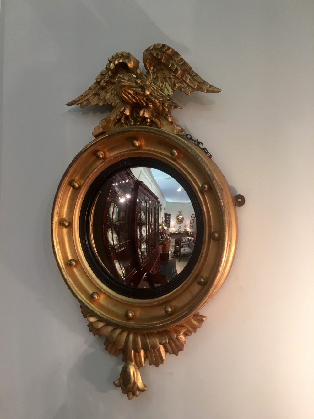 A circular Regency giltwood convex mirror featuring a carved eagle surmount, ball ornamentation along the moulded frame, an ebonised inner slip, and a carved pendant base.