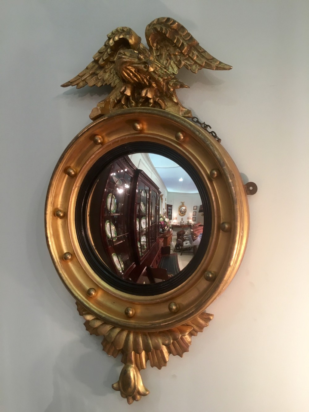 A circular Regency giltwood convex mirror featuring a carved eagle surmount, ball ornamentation along the moulded frame, an ebonised inner slip, and a carved pendant base. View II