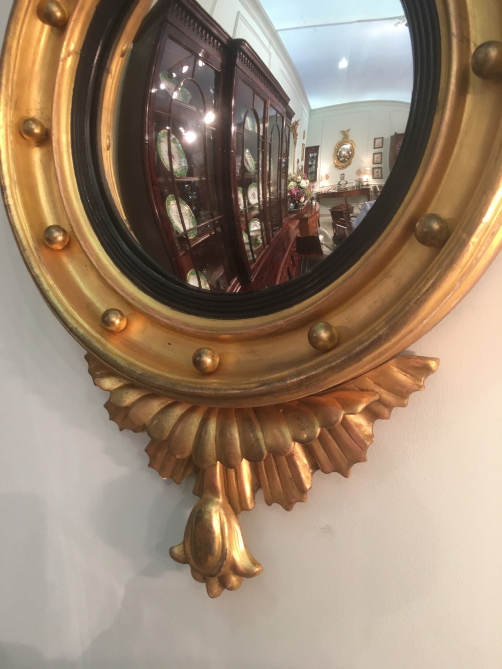 A circular Regency giltwood convex mirror featuring a carved eagle surmount, ball ornamentation along the moulded frame, an ebonised inner slip, and a carved pendant base. View V