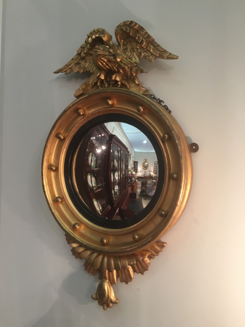 A circular Regency giltwood convex mirror featuring a carved eagle surmount, ball ornamentation along the moulded frame, an ebonised inner slip, and a carved pendant base. View VI