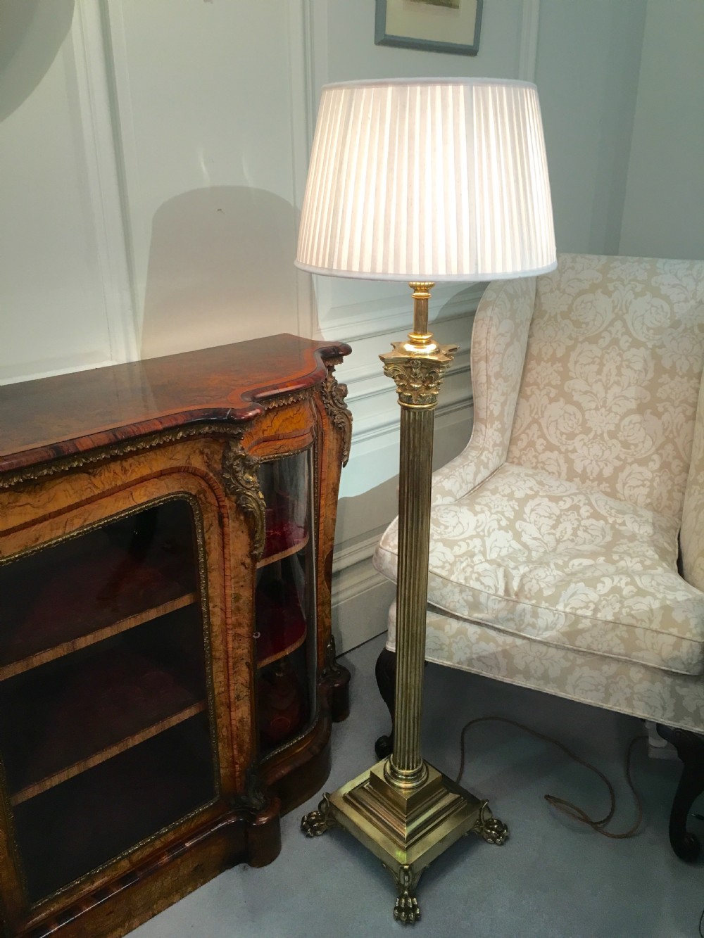 A brass telescopic standard lamp featuring a fluted column stem, Corinthian capital detail, a square stepped base with ornate feet, and a pleated white shade. View II