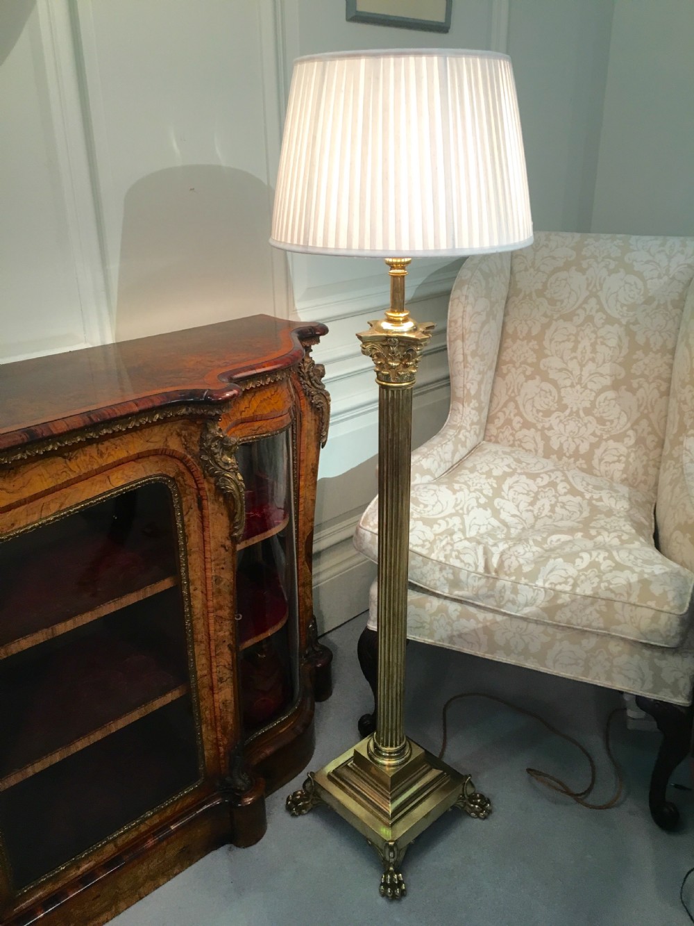 A brass telescopic standard lamp featuring a fluted column stem, Corinthian capital detail, a square stepped base with ornate feet, and a pleated white shade. View III