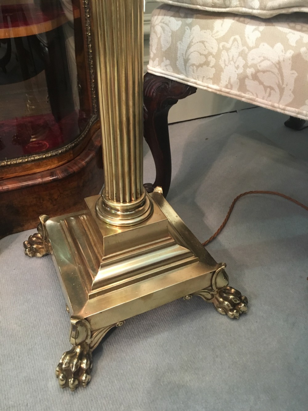 A brass telescopic standard lamp featuring a fluted column stem, Corinthian capital detail, a square stepped base with ornate feet, and a pleated white shade. View VI