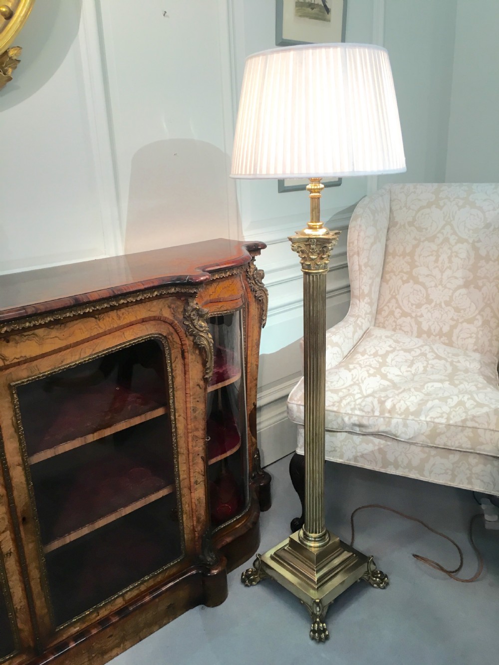 A brass telescopic standard lamp featuring a fluted column stem, Corinthian capital detail, a square stepped base with ornate feet, and a pleated white shade. View XI