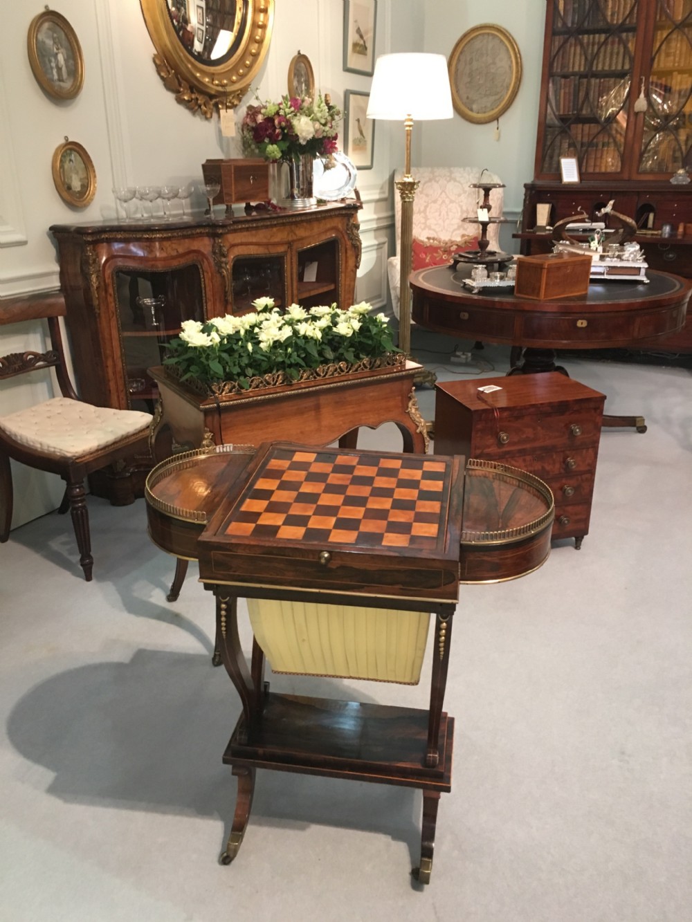 A Regency rosewood games table featuring an inlaid chessboard top, semi-circular brass gallery side tiers, and a pleated silk work bag below. View II