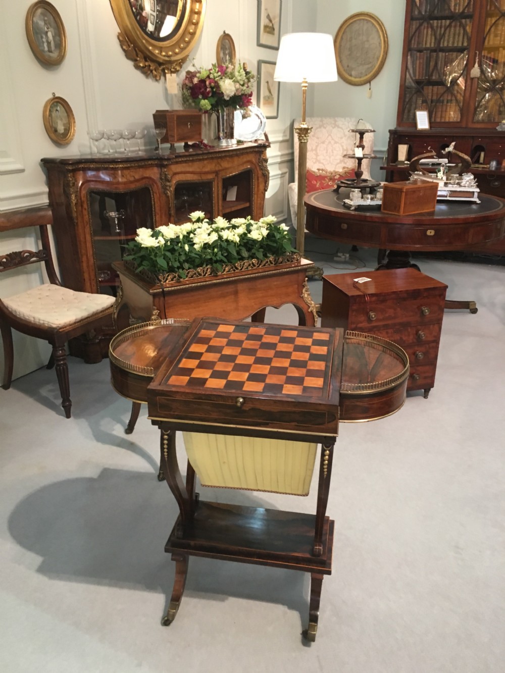 A Regency rosewood games table featuring an inlaid chessboard top, semi-circular brass gallery side tiers, and a pleated silk work bag below. View IV