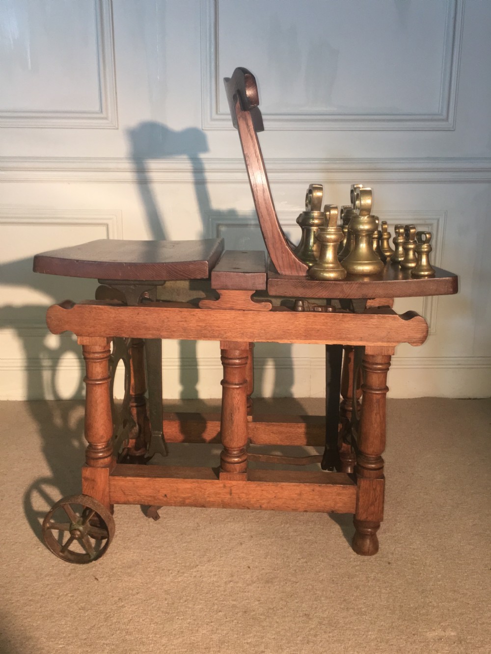 An antique oak jockey scale chair by Young & Son featuring turned legs, rear wheels, a brass balance mechanism, and a set of bell-shaped brass weights. View VIII