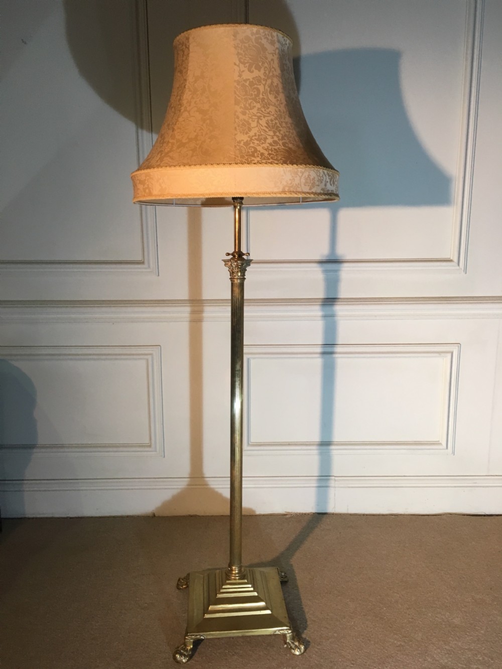 A Victorian brass standard lamp featuring a fluted Corinthian column, an adjustable telescopic shaft, a stepped square base with claw feet, and a patterned fabric shade.