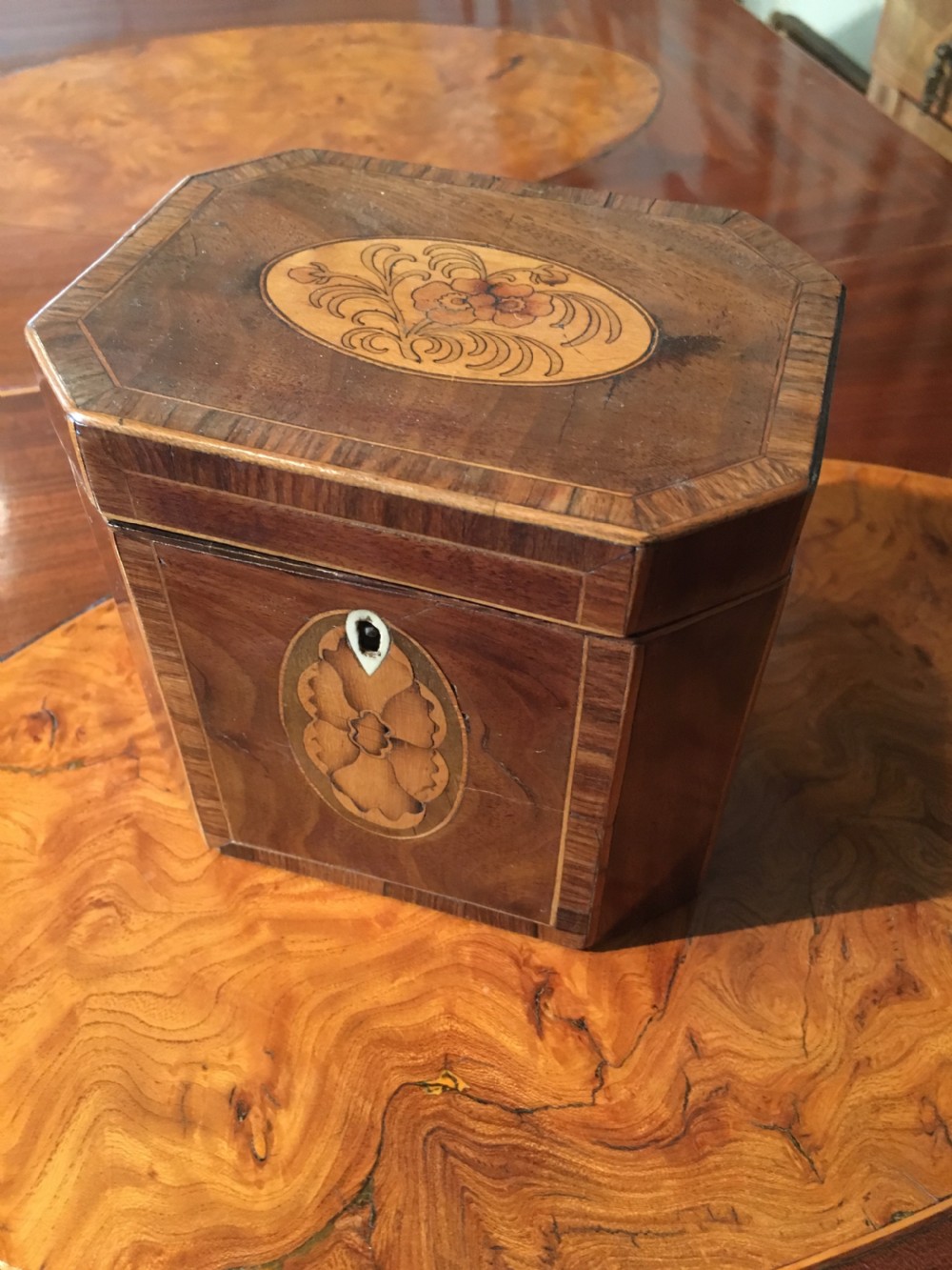 An octagonal George III wooden tea caddy featuring a hinged lid with a central floral marquetry medallion, crossbanded borders, and a matching front escutcheon inlay. View III
