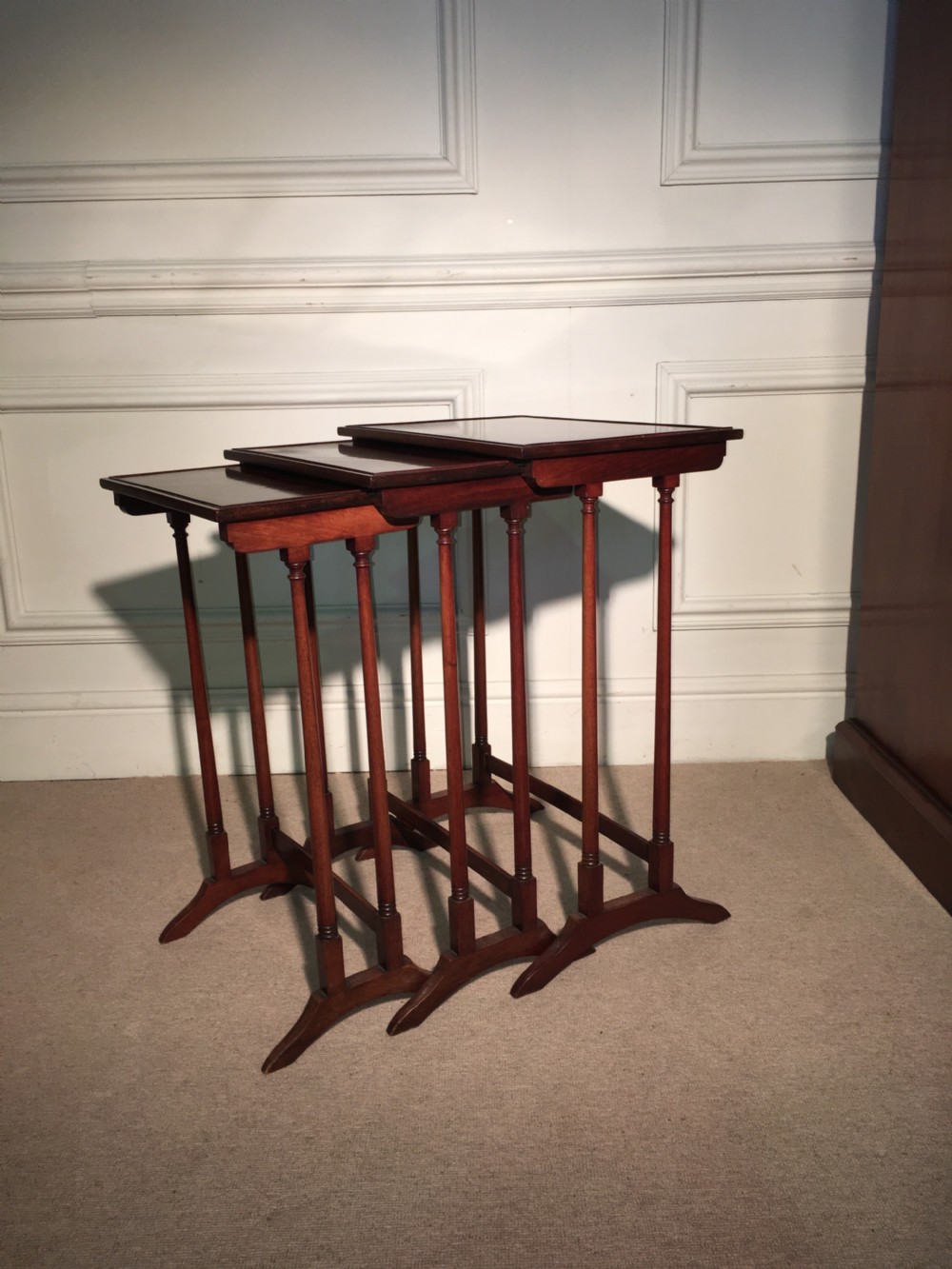 A nest of three mahogany side tables with slender turned spindle legs and splayed feet arranged in a stepped formation.